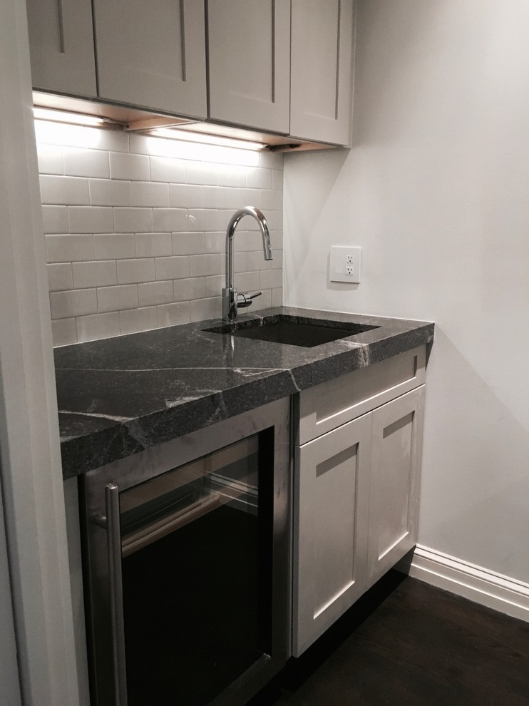 Photo of a contemporary wet bar in Baltimore with a submerged sink, shaker cabinets, grey cabinets, granite worktops, white splashback, metro tiled splashback, dark hardwood flooring and brown floors.