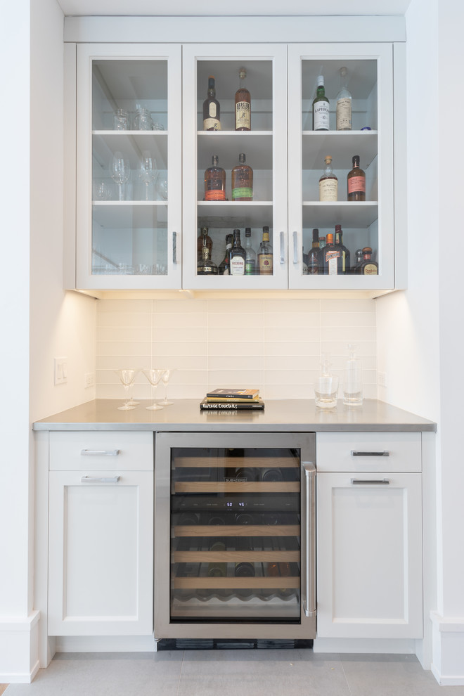 Design ideas for a country single-wall home bar in New York with shaker cabinets, white cabinets, stainless steel worktops, white splashback, glass tiled splashback and grey worktops.