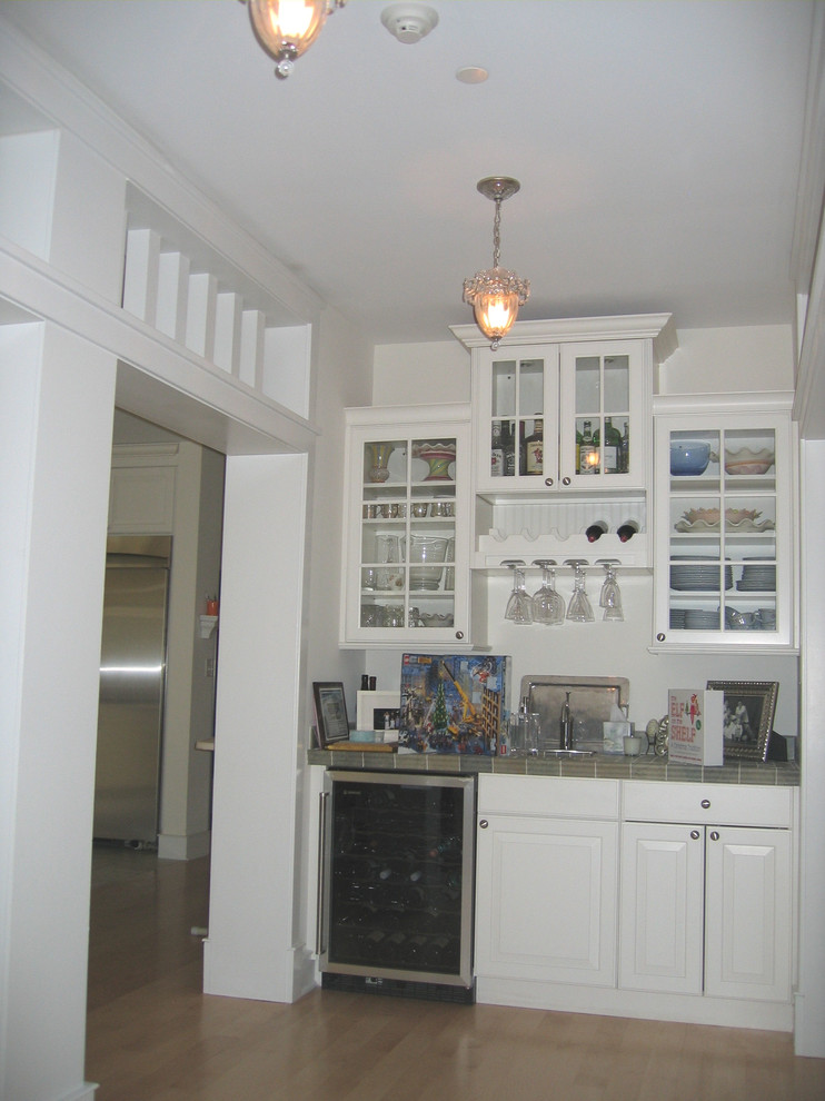 Imagen de bar en casa con fregadero lineal tradicional pequeño con fregadero encastrado, armarios tipo vitrina, puertas de armario blancas, encimera de azulejos y suelo de madera clara