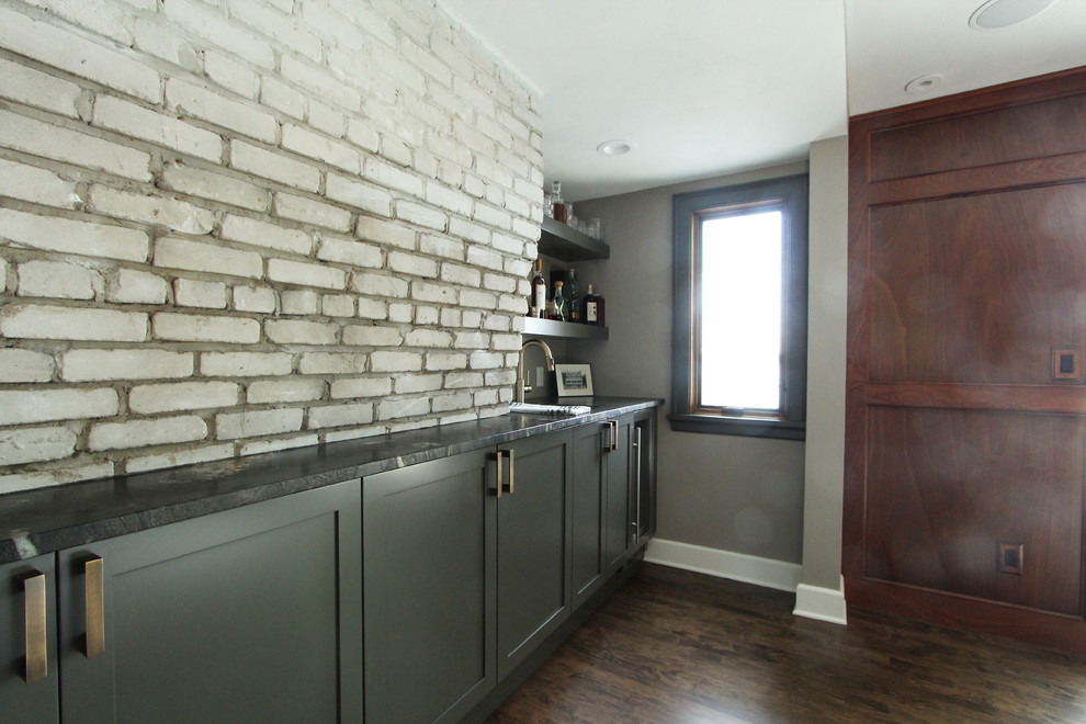 Inspiration for a small classic single-wall wet bar in Other with a submerged sink, shaker cabinets, grey cabinets, granite worktops, dark hardwood flooring, brown floors, black worktops, grey splashback and brick splashback.