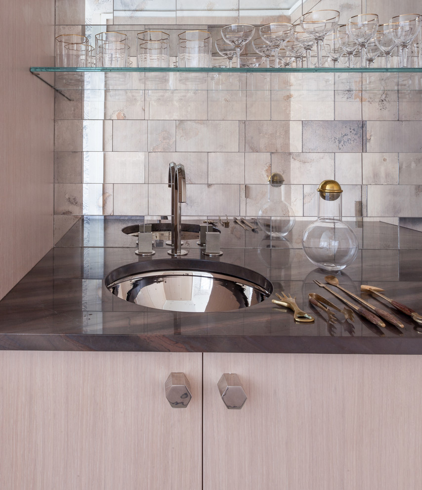 This is an example of a medium sized contemporary single-wall wet bar in New York with a submerged sink, flat-panel cabinets, light wood cabinets, marble worktops, grey splashback, mirror splashback, light hardwood flooring and brown worktops.