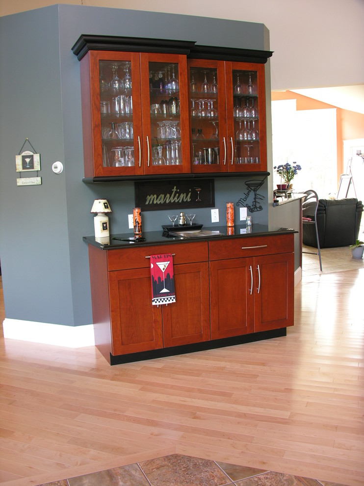 This is an example of a medium sized traditional single-wall wet bar in Portland Maine with no sink, glass-front cabinets, medium wood cabinets, composite countertops and light hardwood flooring.