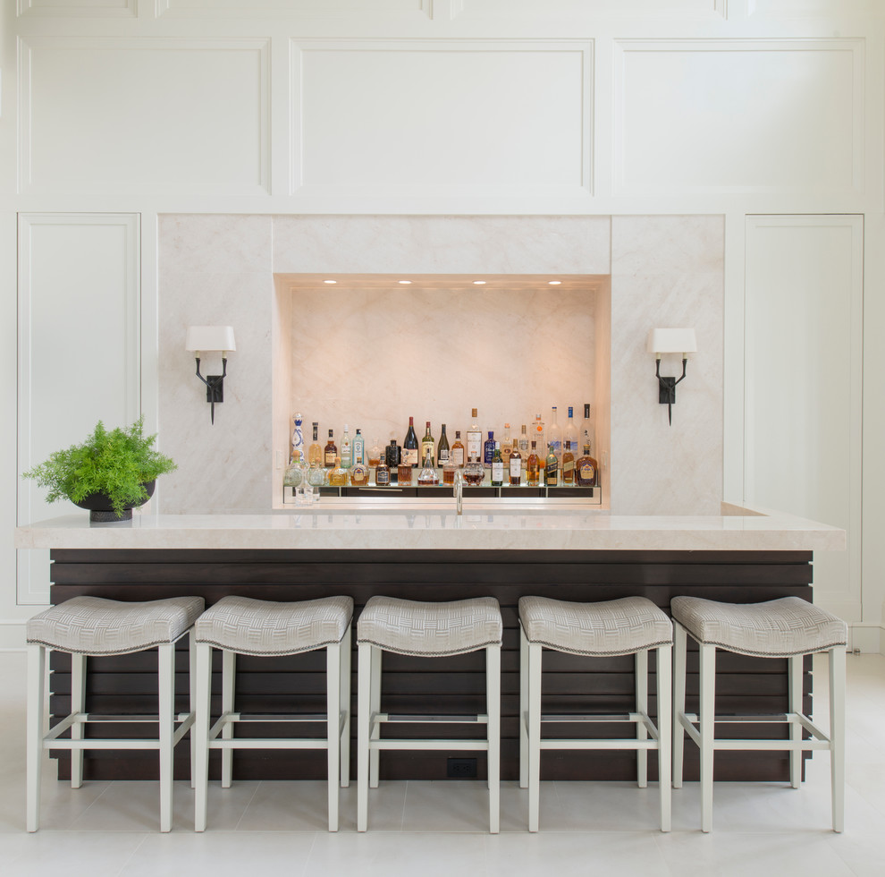 Cette image montre un grand bar de salon linéaire traditionnel avec des tabourets, plan de travail en marbre, une crédence beige, une crédence en dalle de pierre, un évier encastré et un plan de travail blanc.