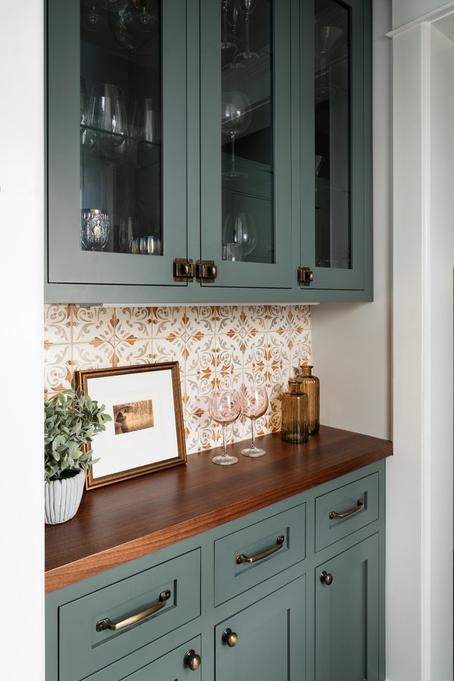 This is an example of a medium sized classic single-wall home bar in New York with glass-front cabinets, green cabinets, wood worktops and terracotta splashback.