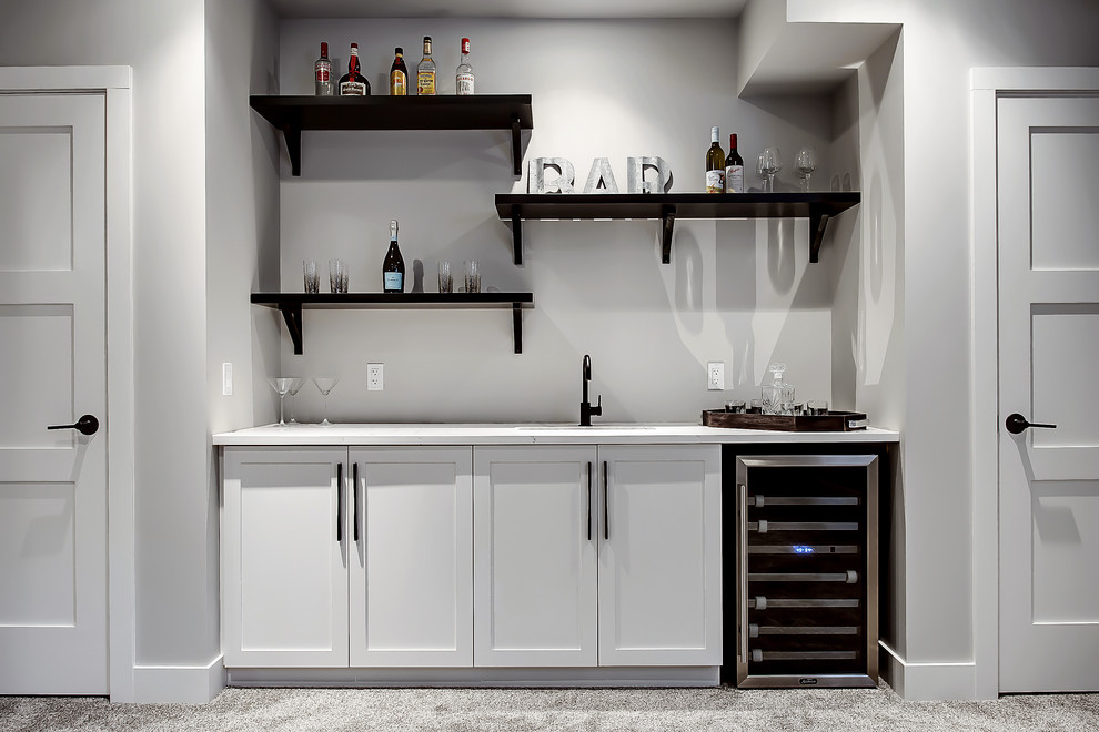 This is an example of a classic single-wall wet bar in Calgary with a submerged sink, shaker cabinets, white cabinets and carpet.