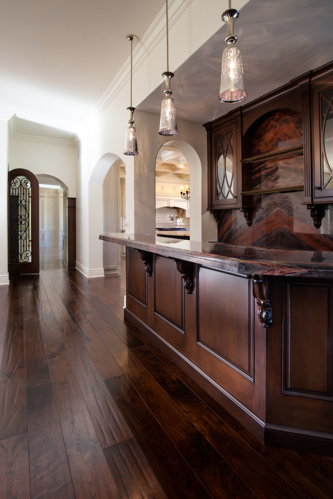 Klassisk inredning av en mellanstor l-formad hemmabar med vask, med en undermonterad diskho, luckor med profilerade fronter, skåp i mörkt trä, marmorbänkskiva, brunt stänkskydd, stänkskydd i sten och mörkt trägolv