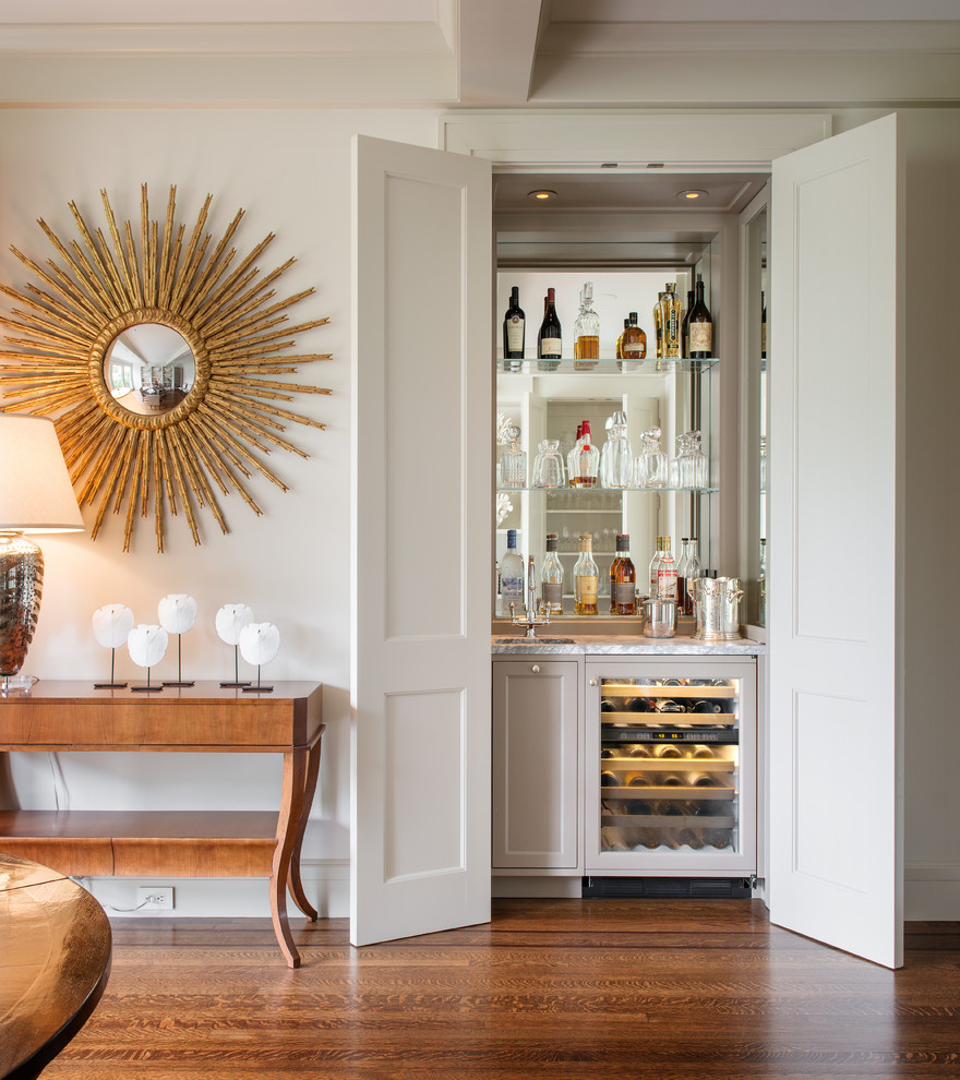 Wet bar - small transitional single-wall medium tone wood floor and brown floor wet bar idea in San Francisco with an undermount sink, recessed-panel cabinets, gray cabinets, mirror backsplash and white countertops
