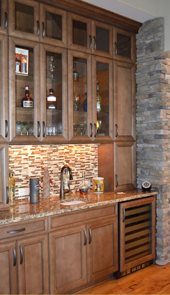 Cette image montre un petit bar de salon avec évier linéaire traditionnel en bois brun avec un évier encastré, un placard avec porte à panneau encastré, un plan de travail en granite, une crédence multicolore, une crédence en carreau briquette, parquet clair et un sol marron.
