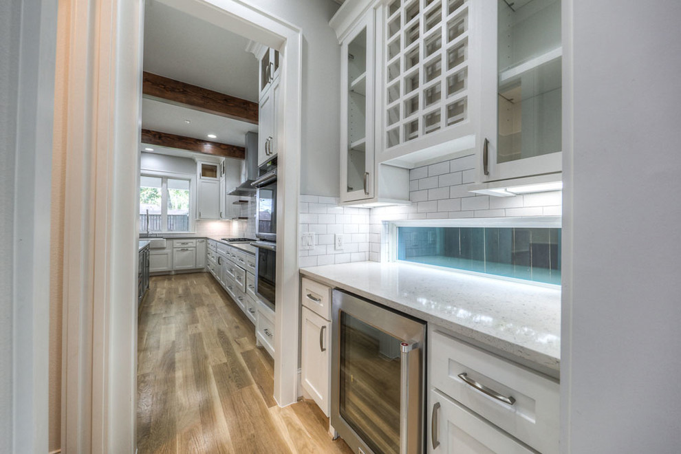Example of a small transitional single-wall light wood floor kitchen design in Houston with glass-front cabinets, white cabinets, quartzite countertops, white backsplash and subway tile backsplash