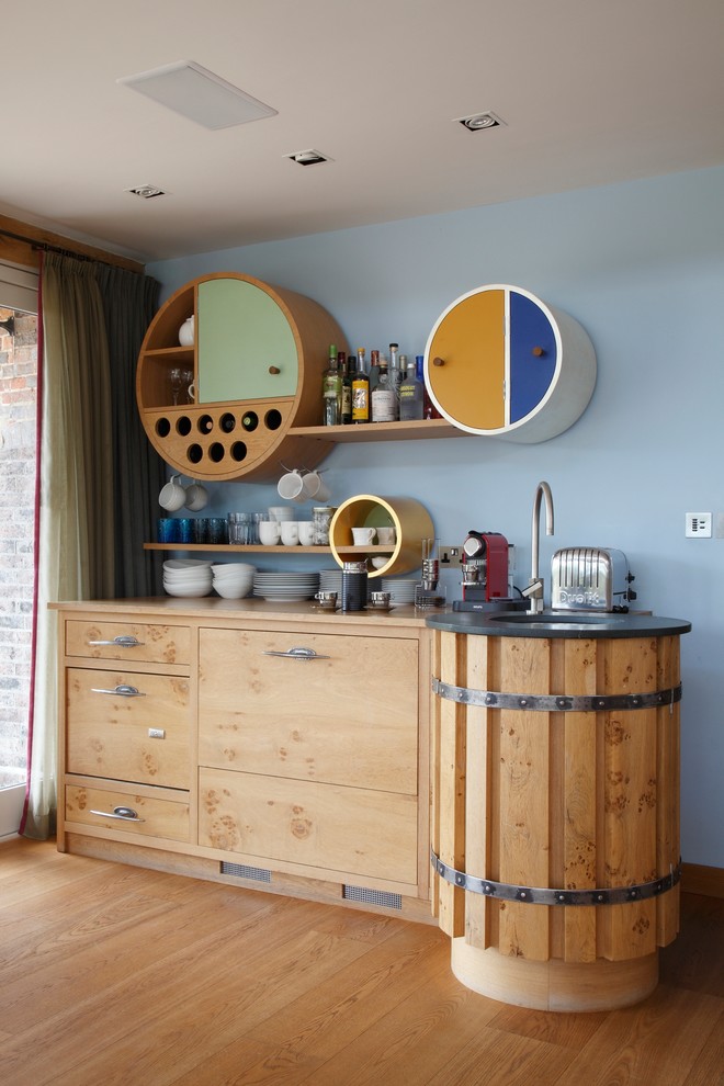 This is an example of a small urban single-wall home bar in Hampshire with a submerged sink, flat-panel cabinets, light wood cabinets and light hardwood flooring.