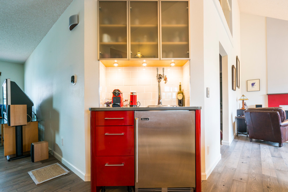 Small contemporary single-wall wet bar in Denver with flat-panel cabinets, red cabinets, engineered stone countertops, white splashback, metro tiled splashback, medium hardwood flooring, brown floors and grey worktops.