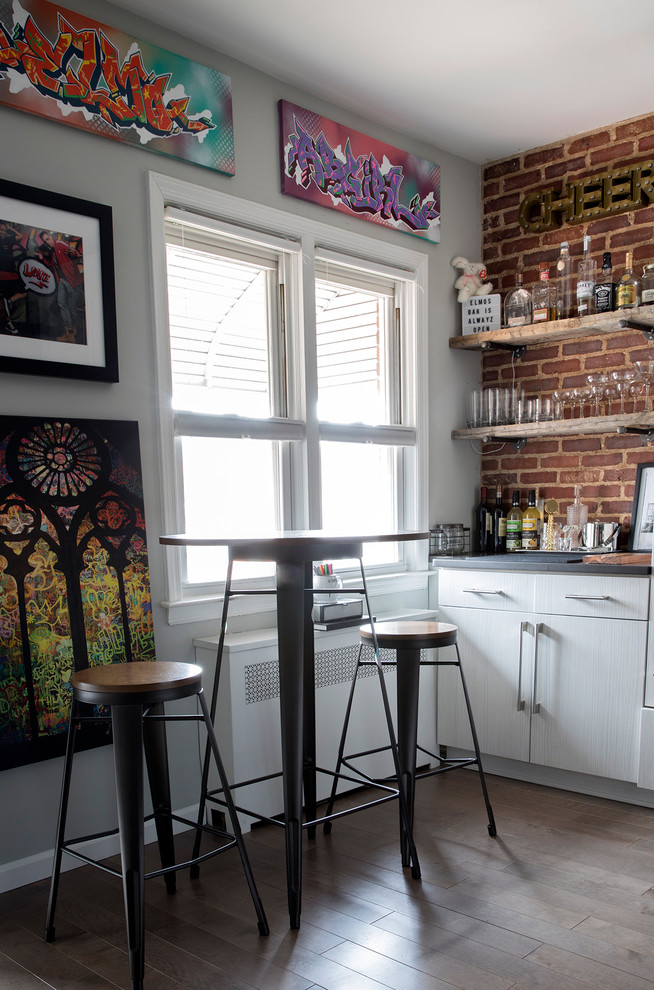 This is an example of a medium sized industrial single-wall wet bar in New York with no sink, flat-panel cabinets, white cabinets, composite countertops, brown splashback, brick splashback, medium hardwood flooring and brown floors.