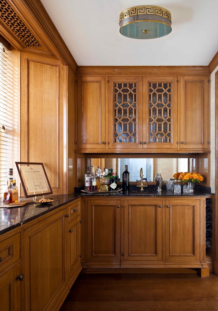 Traditional l-shaped wet bar in New York with a submerged sink, medium wood cabinets, medium hardwood flooring and mirror splashback.