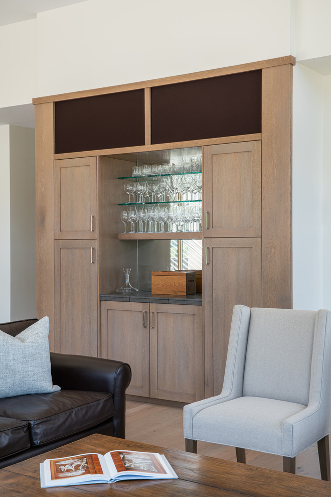 Inspiration for a medium sized classic single-wall home bar in Boise with recessed-panel cabinets, light wood cabinets, granite worktops, mirror splashback, light hardwood flooring, beige floors and grey worktops.