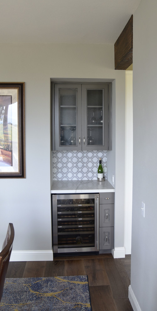 Example of a small cottage single-wall medium tone wood floor and brown floor wet bar design in San Francisco with glass-front cabinets, gray cabinets, quartz countertops, white backsplash and white countertops