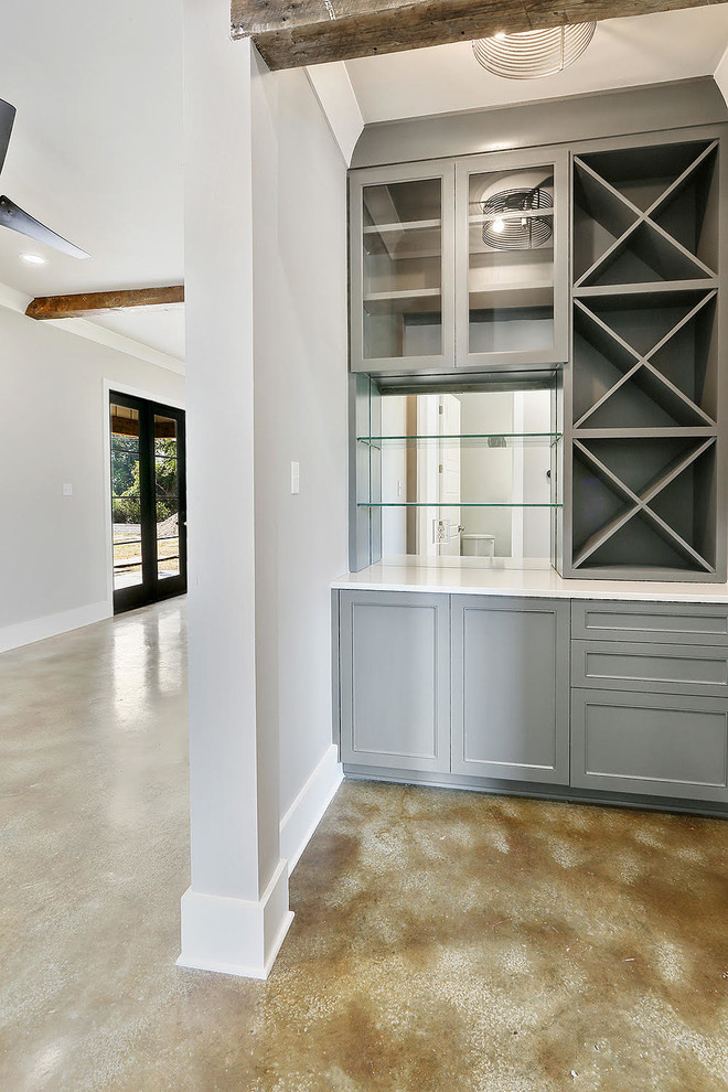 Small trendy single-wall concrete floor and beige floor wet bar photo in New Orleans with no sink, recessed-panel cabinets, gray cabinets, solid surface countertops, multicolored backsplash and mirror backsplash