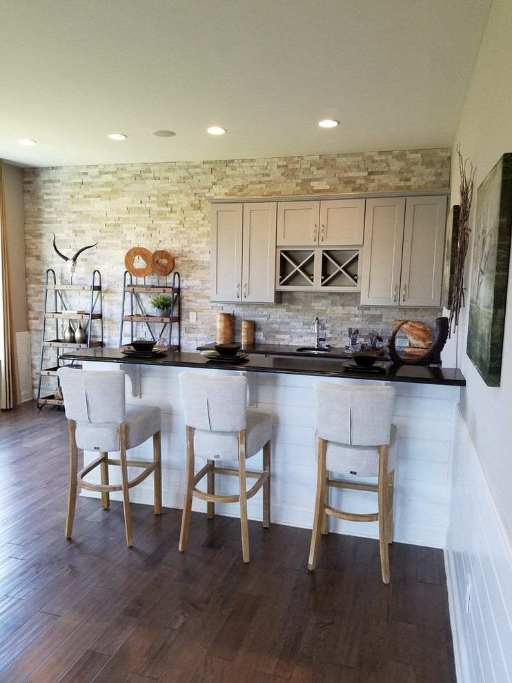 Example of a mid-sized transitional galley dark wood floor and brown floor seated home bar design in Charlotte with an undermount sink, shaker cabinets, beige cabinets, granite countertops, beige backsplash and stone tile backsplash