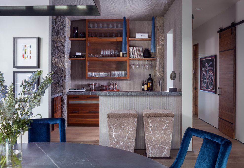 Diseño de bar en casa con barra de bar rústico con armarios abiertos, puertas de armario de madera oscura, suelo de madera clara, suelo beige y encimeras grises