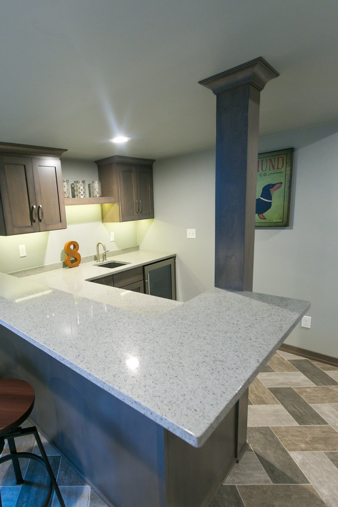 Photo of a large classic l-shaped wet bar in Other with a submerged sink, recessed-panel cabinets, dark wood cabinets, engineered stone countertops, stone slab splashback and vinyl flooring.