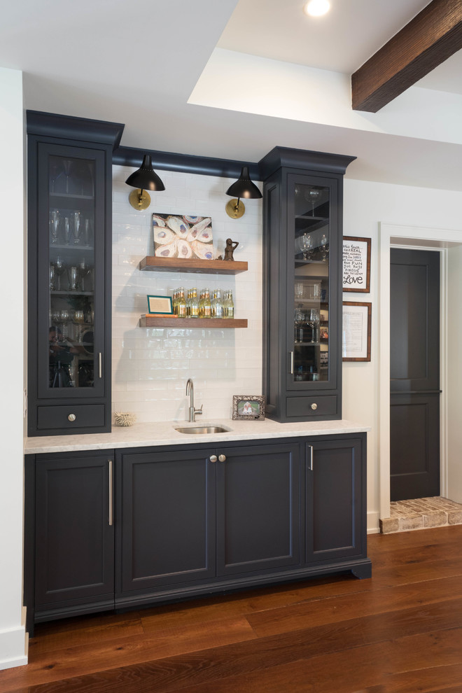 Mid-sized country single-wall dark wood floor and brown floor wet bar photo in Other with an undermount sink, beaded inset cabinets, gray cabinets, marble countertops, white backsplash, subway tile backsplash and gray countertops