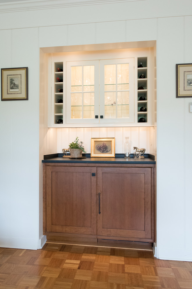 Example of a small classic single-wall light wood floor and brown floor home bar design in Philadelphia with beaded inset cabinets, medium tone wood cabinets, soapstone countertops, white backsplash, wood backsplash and black countertops