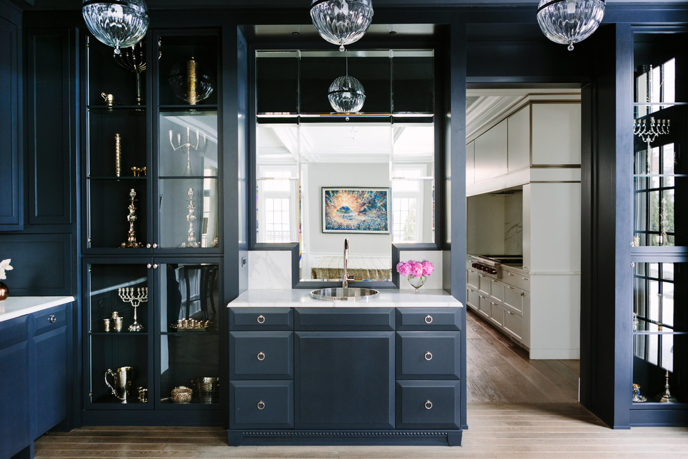 Klassisk inredning av en stor vita vitt hemmabar med vask, med en nedsänkt diskho, blå skåp, marmorbänkskiva, spegel som stänkskydd, luckor med upphöjd panel och mellanmörkt trägolv