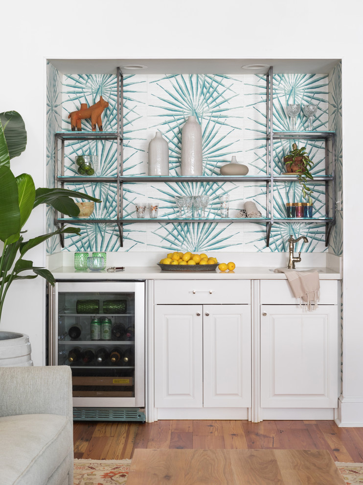 Wet bar - transitional single-wall medium tone wood floor wet bar idea in New Orleans with an undermount sink, raised-panel cabinets, white cabinets, multicolored backsplash and white countertops