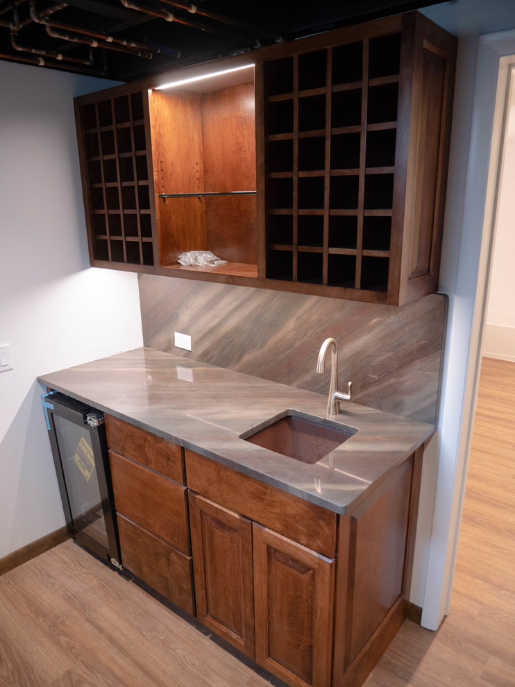 Inspiration for a mid-sized contemporary single-wall medium tone wood floor and brown floor wet bar remodel in St Louis with a drop-in sink, raised-panel cabinets, medium tone wood cabinets, laminate countertops, multicolored backsplash and multicolored countertops