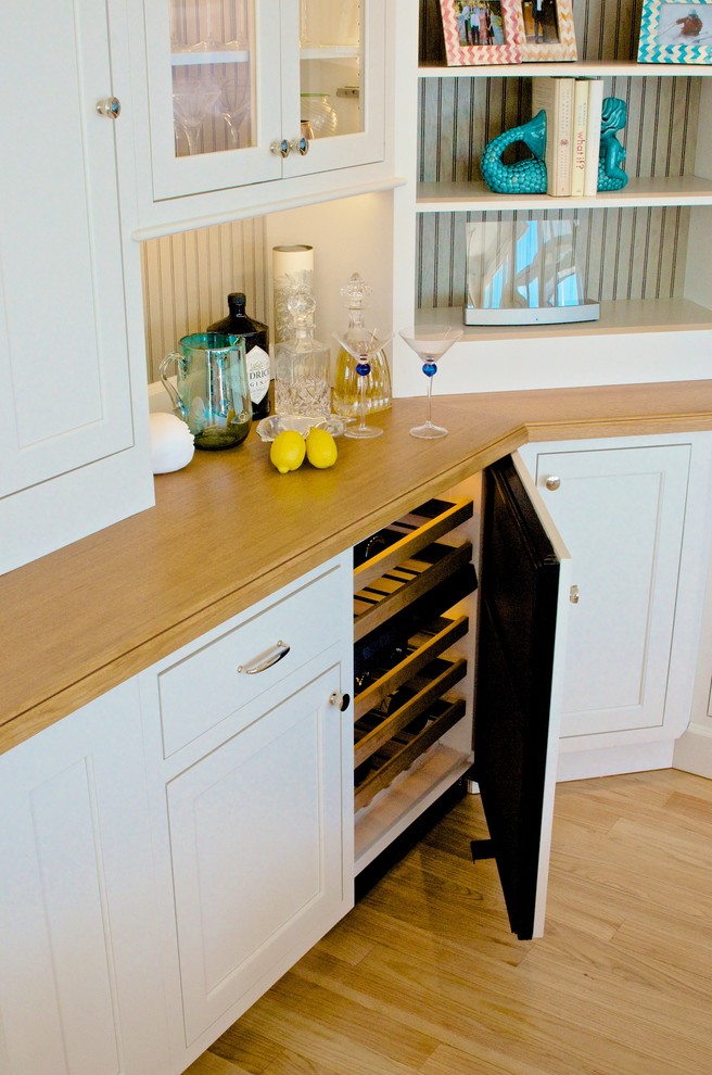 Photo of a medium sized nautical l-shaped wet bar in Boston with no sink, shaker cabinets, white cabinets, wood worktops, beige splashback and light hardwood flooring.