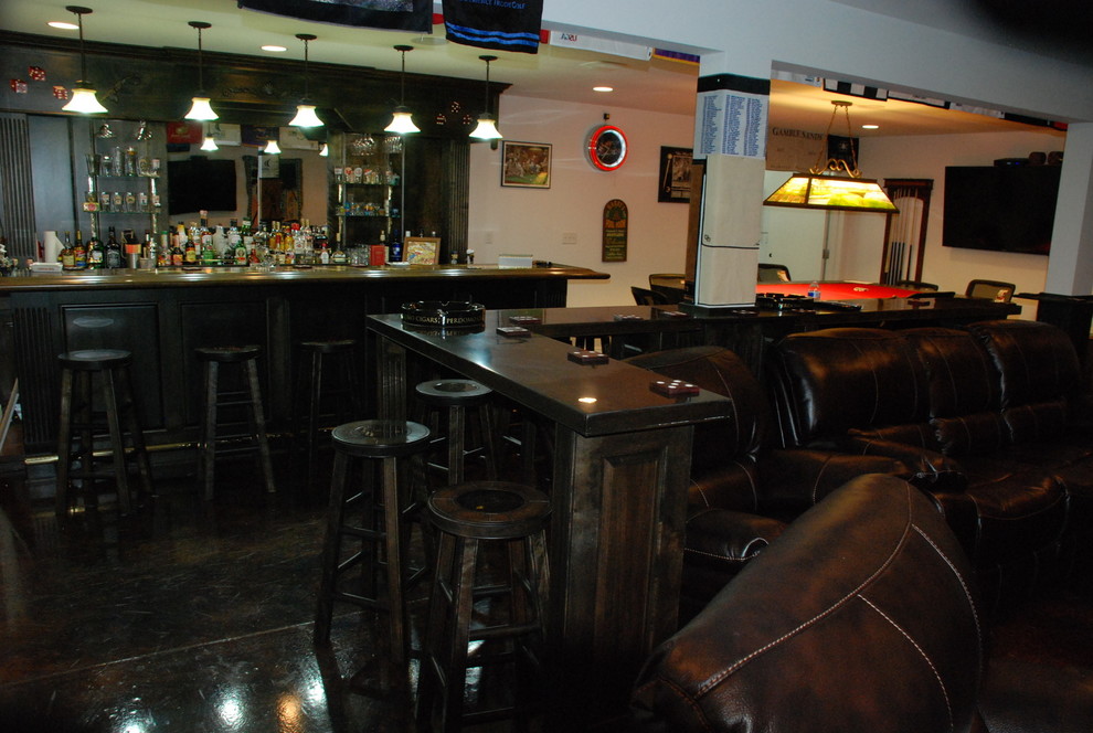 Idee per un grande bancone bar classico con ante con bugna sagomata, ante in legno bruno, top in legno, paraspruzzi a specchio e pavimento in cemento
