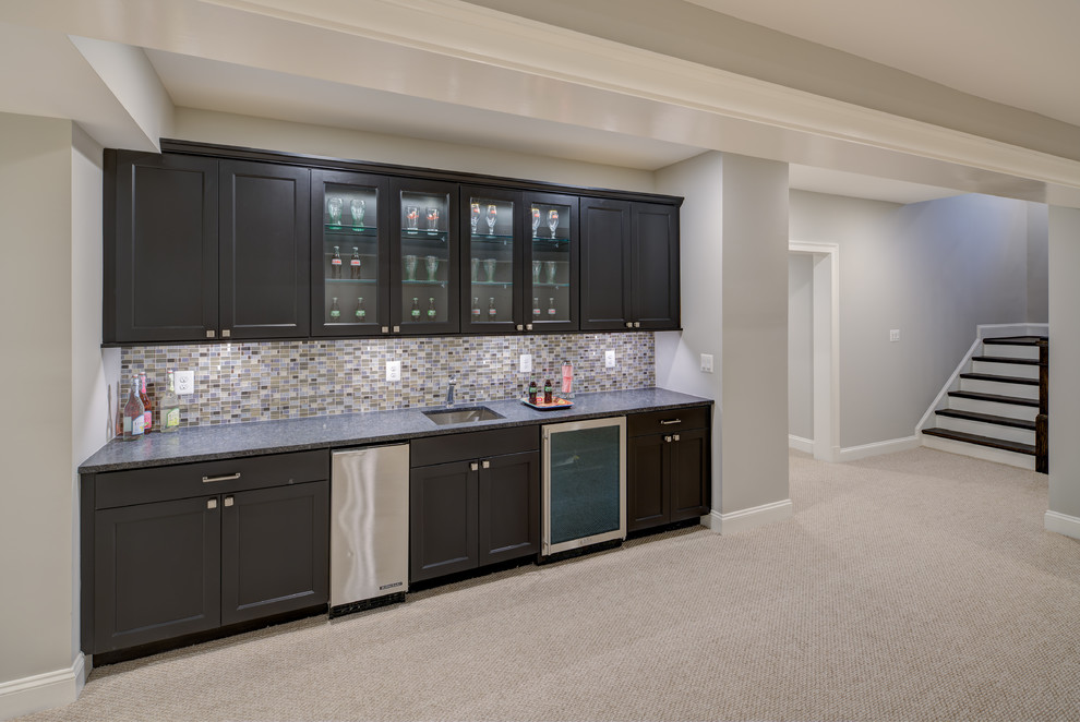 Large traditional single-wall wet bar in DC Metro with a submerged sink, shaker cabinets, dark wood cabinets, granite worktops, grey splashback, glass tiled splashback, carpet and grey floors.