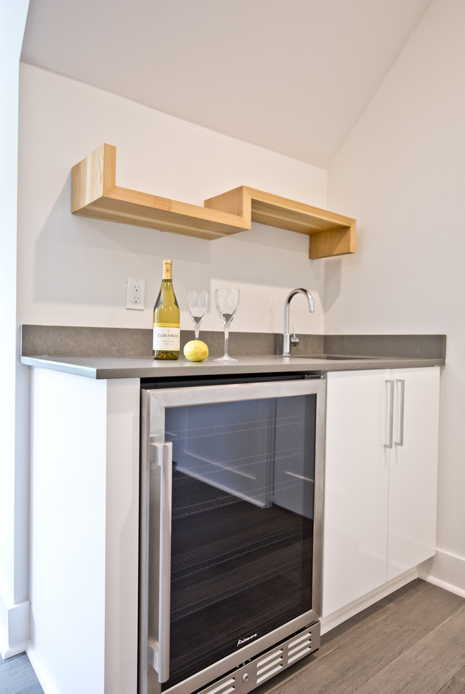 Inspiration for a small contemporary single-wall wet bar in Other with a submerged sink, flat-panel cabinets, white cabinets, engineered stone countertops, medium hardwood flooring, brown floors and grey worktops.