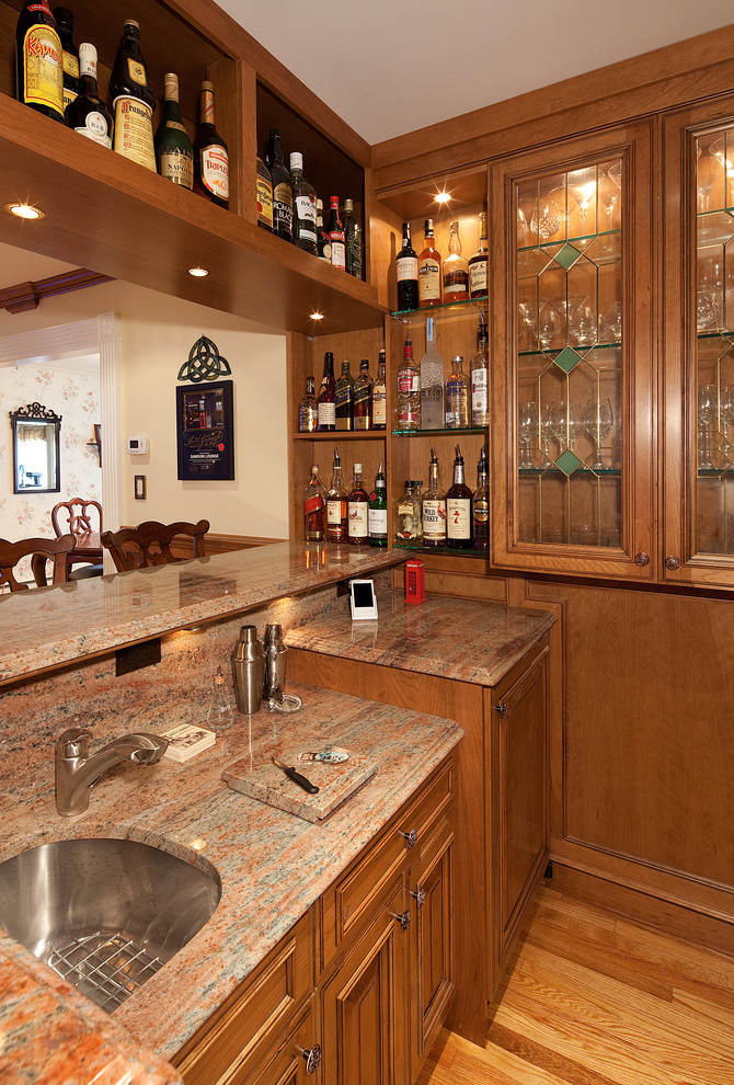 Inspiration for a mid-sized timeless l-shaped medium tone wood floor wet bar remodel in New York with an undermount sink, raised-panel cabinets, medium tone wood cabinets, granite countertops, brown backsplash and stone slab backsplash