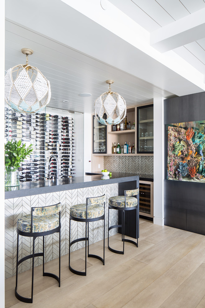 Inspiration for a coastal breakfast bar in Orange County with glass-front cabinets, light wood cabinets, white splashback, light hardwood flooring, beige floors, grey worktops and feature lighting.