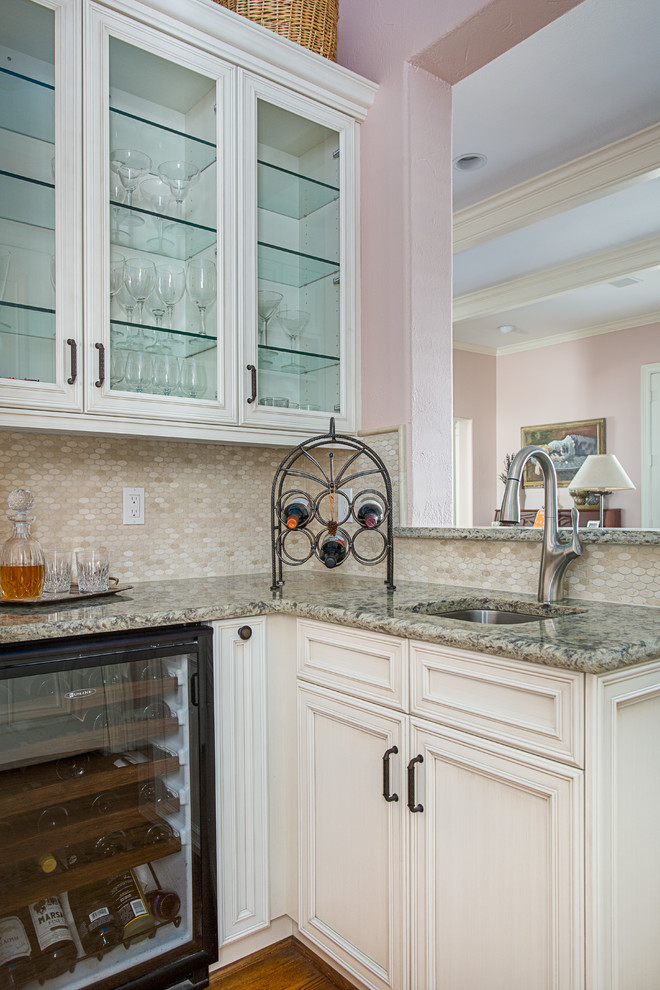 Small l-shaped wet bar in Dallas with a submerged sink, flat-panel cabinets, beige cabinets, engineered stone countertops, beige splashback, marble splashback, medium hardwood flooring, brown floors and grey worktops.