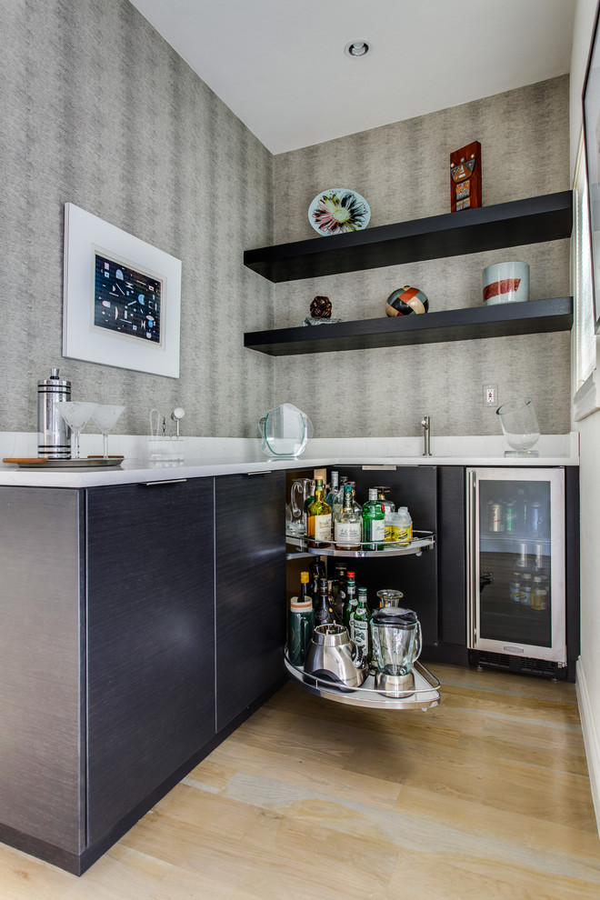 This is an example of a medium sized contemporary u-shaped home bar in Dallas with flat-panel cabinets, grey cabinets, engineered stone countertops, white splashback and light hardwood flooring.