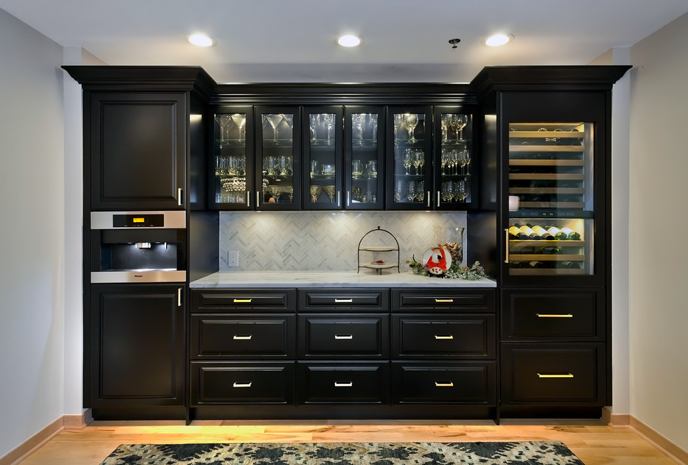 This is an example of a medium sized traditional single-wall home bar in Minneapolis with raised-panel cabinets, black cabinets, marble worktops, white splashback, stone tiled splashback and light hardwood flooring.