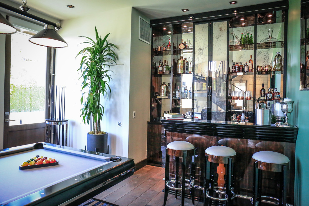 Cette photo montre un grand bar de salon parallèle avec des tabourets, un placard à porte vitrée, des portes de placard marrons, un plan de travail en verre, une crédence en feuille de verre, un sol en bois brun et plan de travail noir.