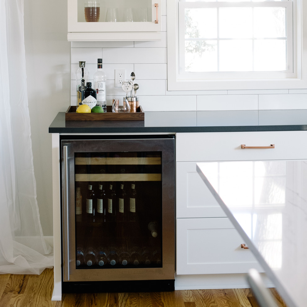 Design ideas for a small home bar in Minneapolis with no sink, white cabinets, engineered stone countertops, white splashback, metro tiled splashback and medium hardwood flooring.