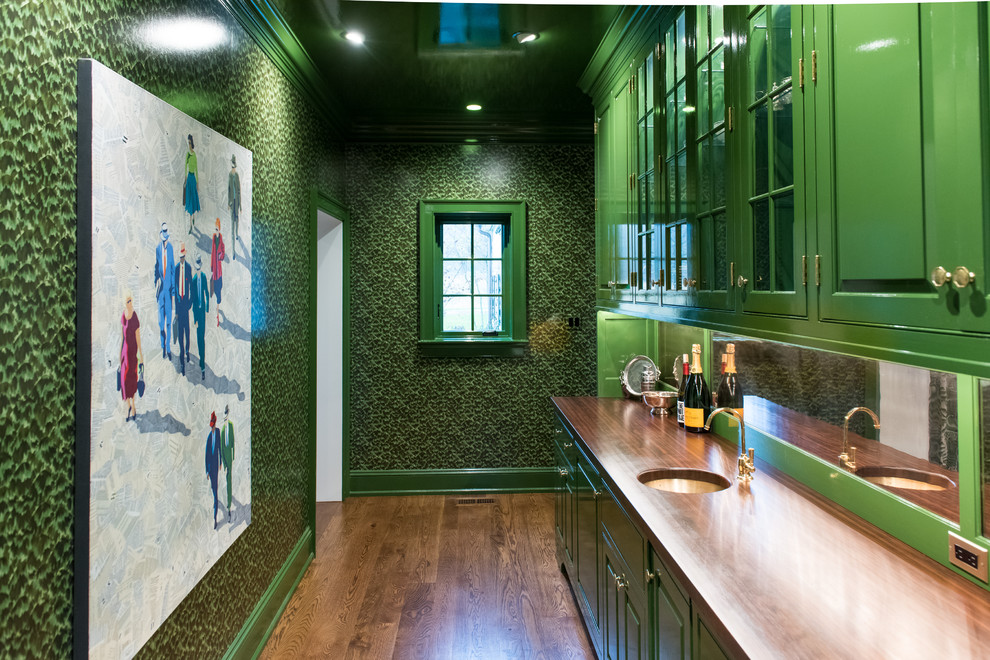 Exempel på en stor klassisk bruna parallell brunt hemmabar med vask, med en undermonterad diskho, luckor med upphöjd panel, gröna skåp, träbänkskiva, spegel som stänkskydd, mellanmörkt trägolv och brunt golv