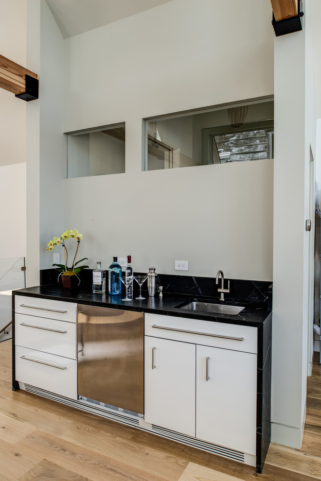 This is an example of a contemporary single-wall wet bar in San Francisco with a submerged sink, flat-panel cabinets, white cabinets and medium hardwood flooring.