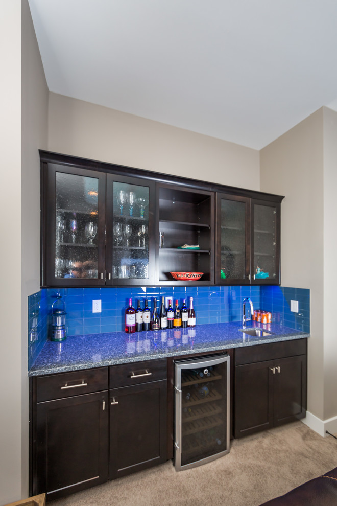 This is an example of a large traditional single-wall wet bar in Jacksonville with a submerged sink, shaker cabinets, dark wood cabinets, engineered stone countertops, blue splashback, glass tiled splashback and carpet.