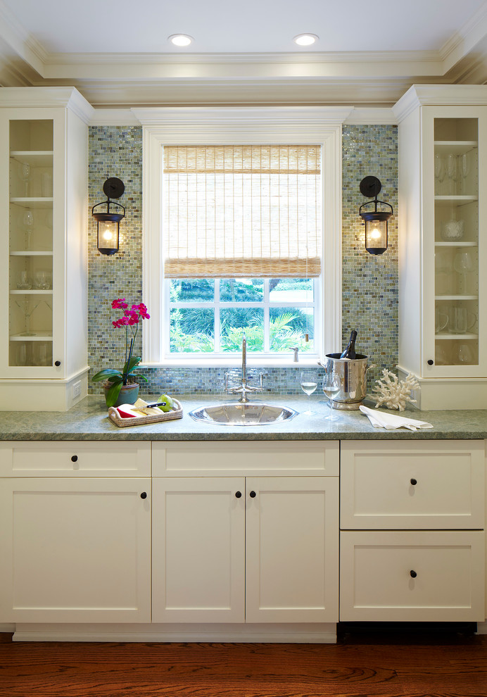 Klassisk inredning av en mellanstor linjär hemmabar med vask, med vita skåp, vitt stänkskydd, mellanmörkt trägolv, brunt golv, en nedsänkt diskho, skåp i shakerstil och stänkskydd i stenkakel