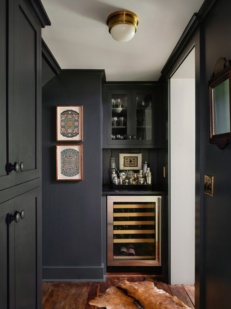 Inredning av en klassisk svarta svart hemmabar med vask, med luckor med glaspanel, svarta skåp, svart stänkskydd, mörkt trägolv och brunt golv