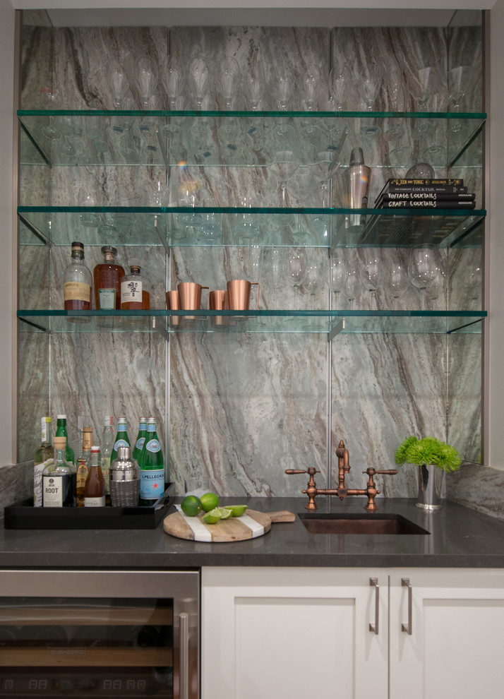 Photo of a traditional single-wall wet bar in New York with a built-in sink, shaker cabinets, white cabinets, engineered stone countertops, grey splashback, marble splashback, medium hardwood flooring and brown floors.