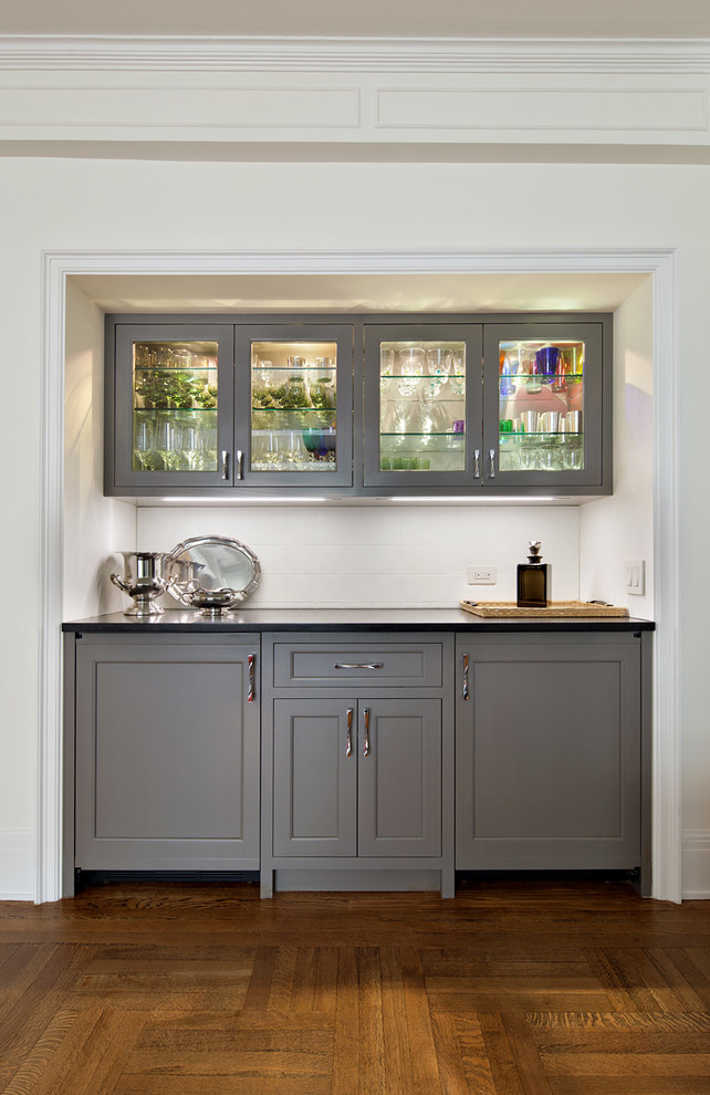 Inspiration for a small classic single-wall wet bar in New York with grey cabinets, granite worktops, white splashback, light hardwood flooring, no sink, beaded cabinets and ceramic splashback.