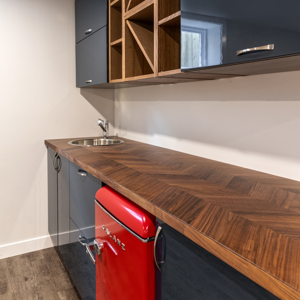 This is an example of a medium sized traditional single-wall wet bar in Edmonton with a built-in sink, flat-panel cabinets, blue cabinets, wood worktops, laminate floors, grey floors and brown worktops.