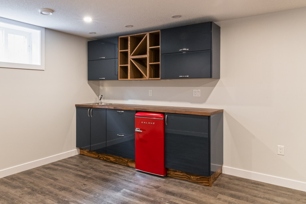This is an example of a medium sized classic single-wall wet bar in Edmonton with grey floors, a built-in sink, flat-panel cabinets, blue cabinets, wood worktops, laminate floors and brown worktops.