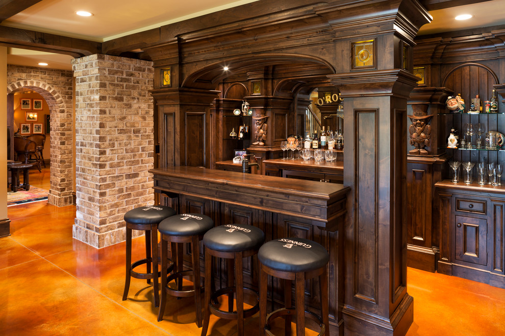 Cette image montre un grand bar de salon parallèle traditionnel en bois foncé avec sol en béton ciré, des tabourets, un placard avec porte à panneau encastré, un plan de travail en bois, un sol orange, une crédence miroir et un plan de travail marron.