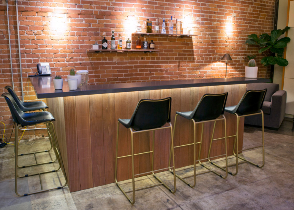 Example of a mid-sized urban l-shaped concrete floor and gray floor seated home bar design in Los Angeles with open cabinets, solid surface countertops, red backsplash and brick backsplash
